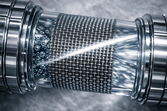 Close-up of a metallic mesh filter with water spraying through it inside a pipe.