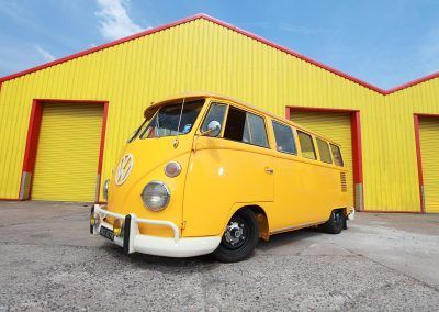 Yellow vintage van parked in front of a yellow building with red trim and garage doors
