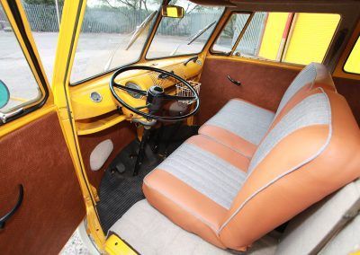 Yellow car interior with tan-and-gray bench seat and steering wheel inside a vintage vehicle