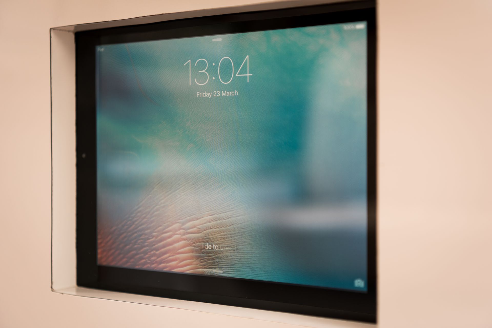 Wall-mounted digital display with a blue-green abstract background and white time text