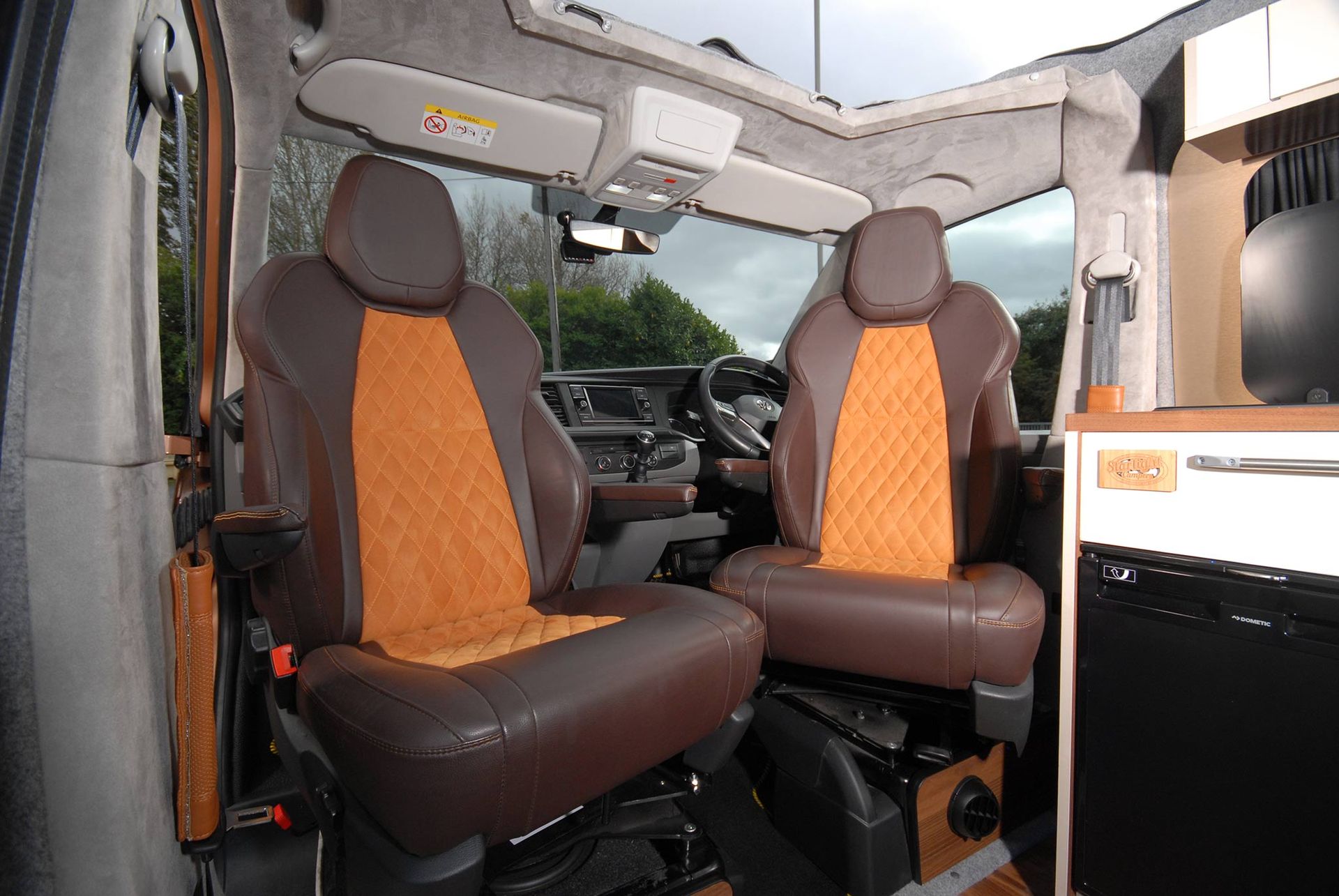 Interior of a vehicle cab with orange and black seats and a view through the windshield