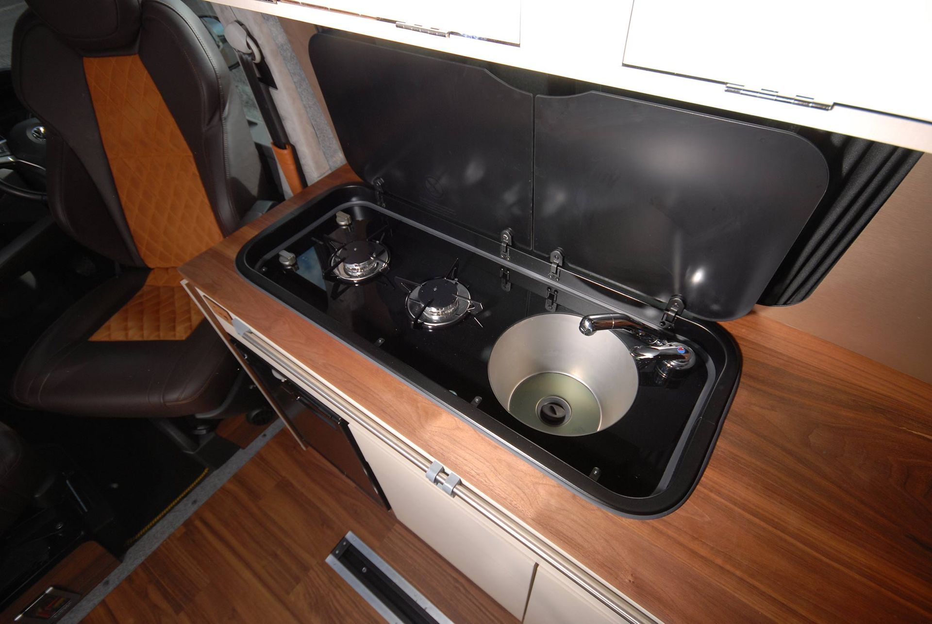 A car center console with a built-in sink, faucet, and wooden trim, next to a black seat.