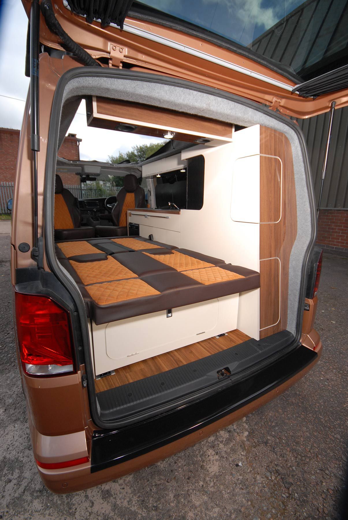 Open camper van interior with fold-out bed and storage, viewed from the rear hatch