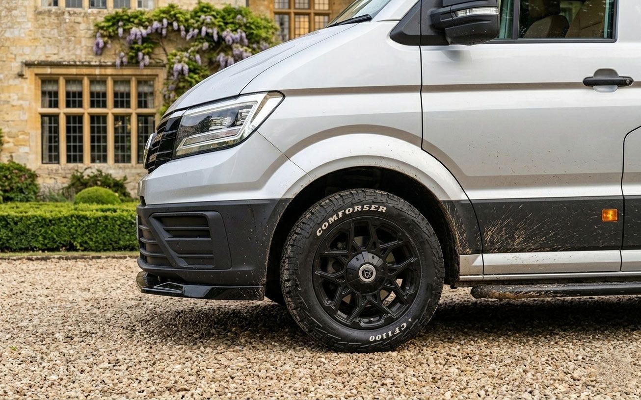 Silver van parked beside a stone house with black wheels and a gravel driveway