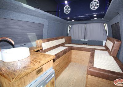 Interior of a custom van conversion with wood seating, white cushions, and ceiling lights