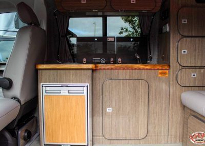 Camper van interior with wood-paneled cabinetry, small fridge, and bench seating