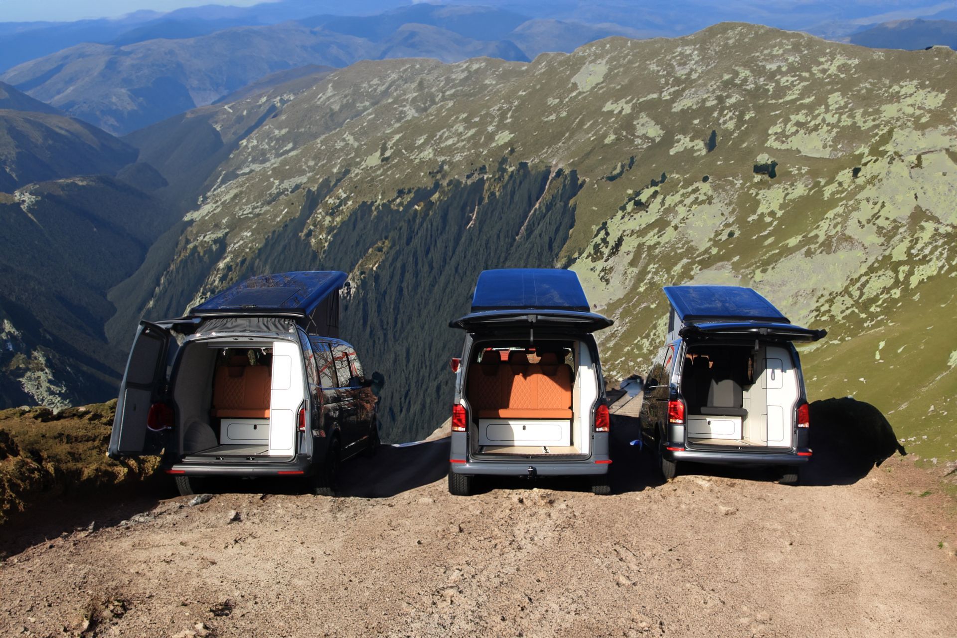 Three parked vans on a mountain overlook with a wide valley view in the background