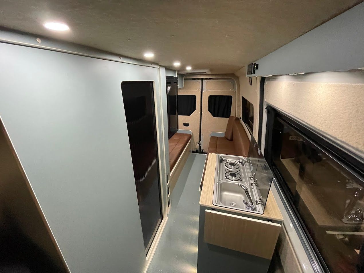 Interior of a narrow camper van with a bed, skylights, and a small kitchenette along the side.