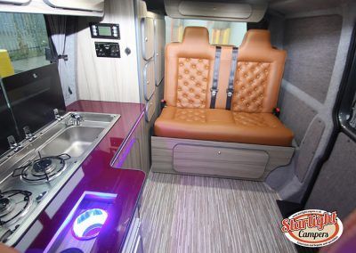 Compact camper van interior with tan bench seats, kitchenette, and purple accent lighting