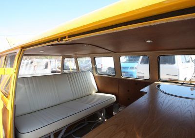 Interior of a vintage van with wood paneling, a white bench seat, and a yellow roof open to the sky