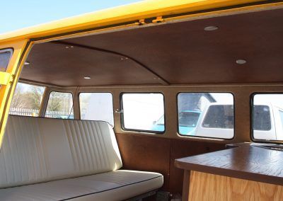 Interior of a vintage camper van with beige bench seating, wooden paneling, and windows.
