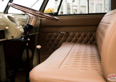 Tan interior of a vintage car with quilted bench seat and steering wheel visible
