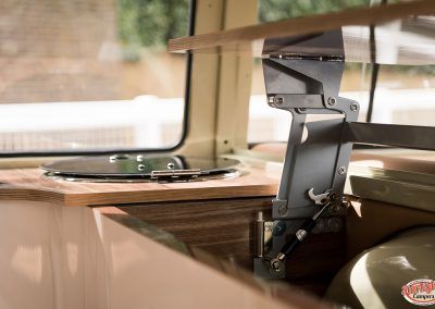 Fold-down table bracket in a camper van beside a window, with a phone resting on the wooden surface.