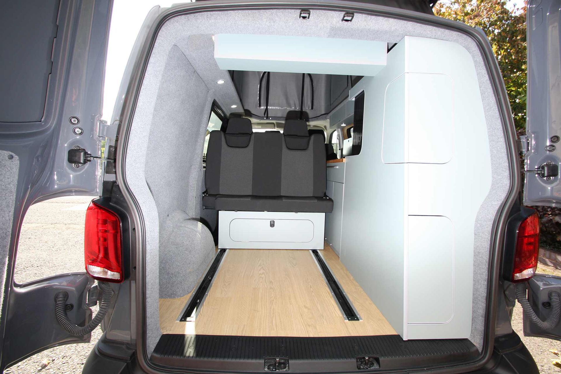 Open van rear cargo area with a wood floor, white cabinet, and gray seating inside.