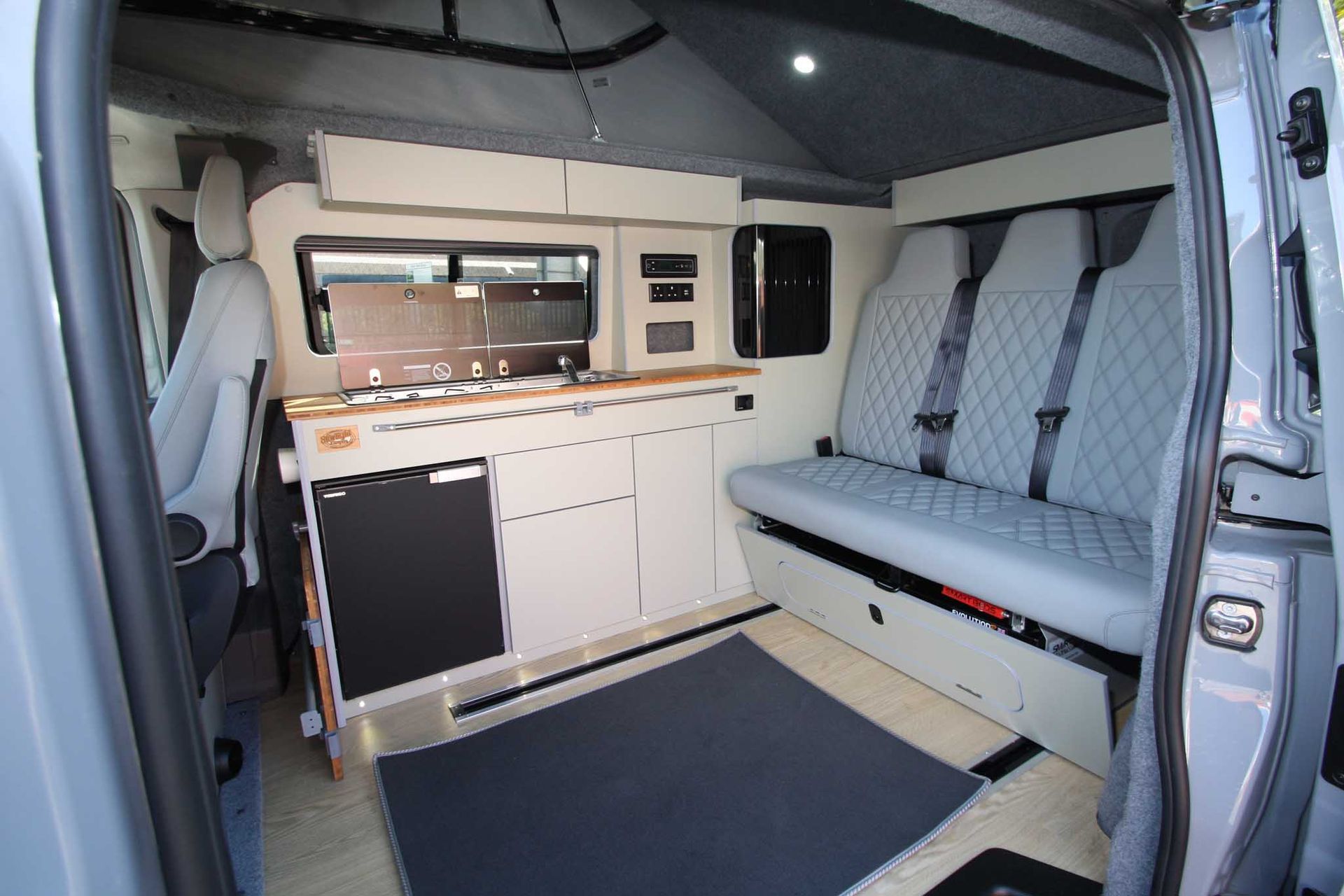 Interior of a camper van with a white cabinet kitchen and gray bench seat