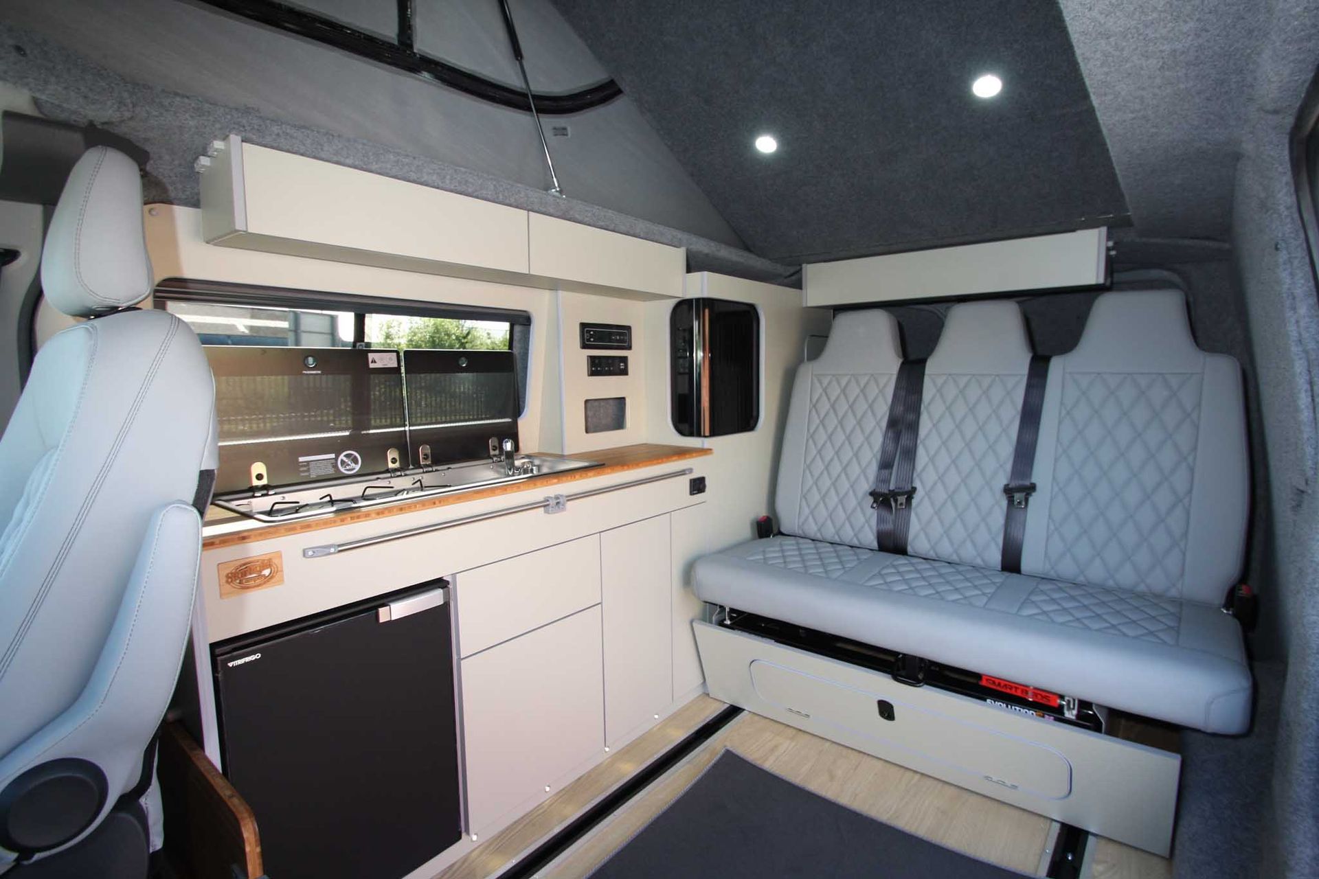 Modern camper van interior with white cabinetry, bench seat, and overhead lights