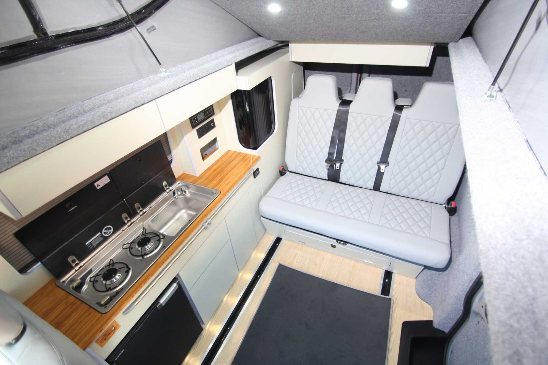 Compact camper van interior with kitchenette, bench seat, and fold-down table under skylights