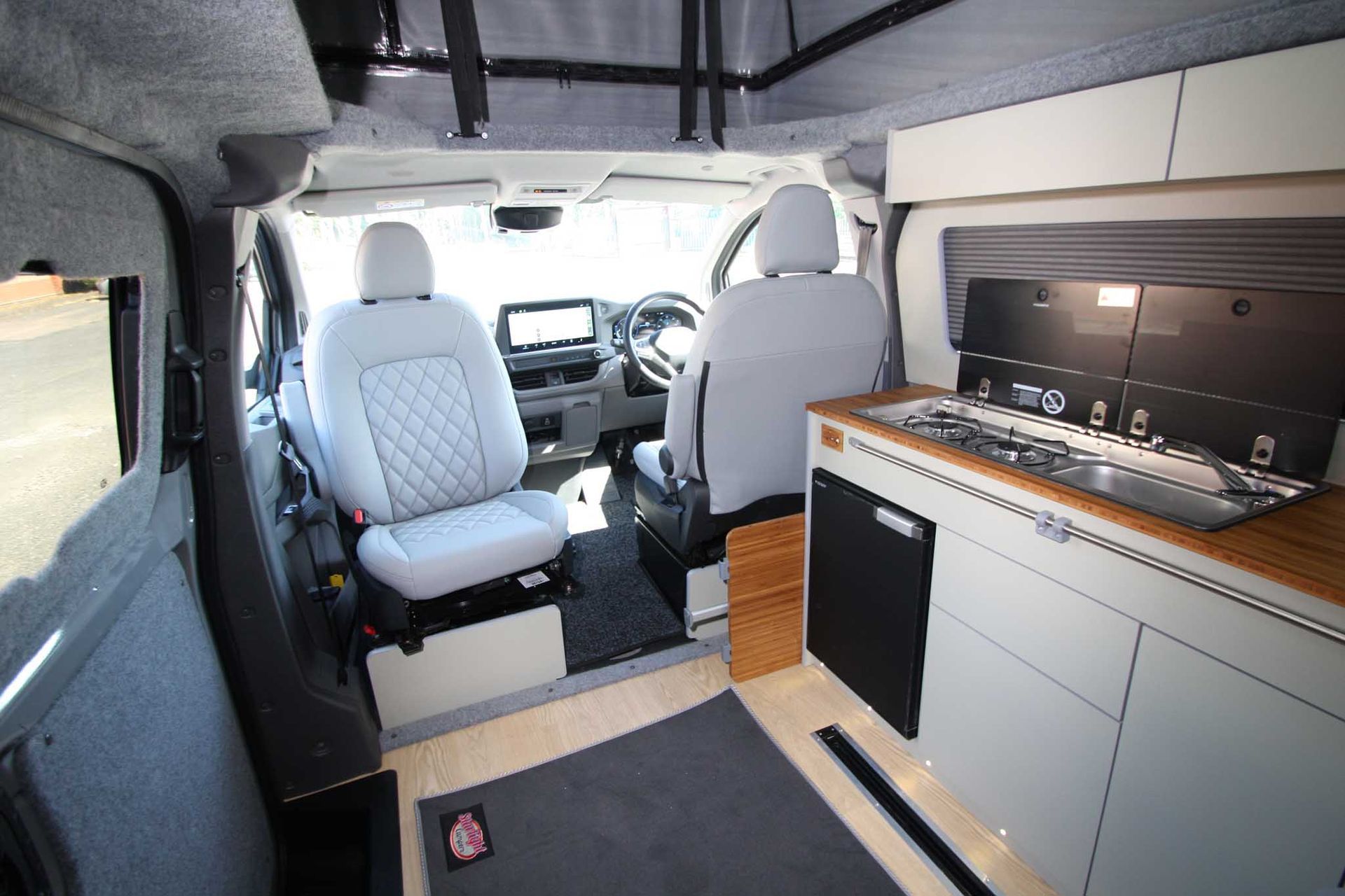 Modern van interior with white seats, wood cabinetry, and a compact kitchen counter
