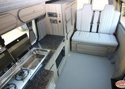 Camper van interior with kitchenette, cabinetry, and two bench seats