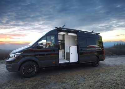 Black camper van with open side door parked at sunset on a scenic overlook