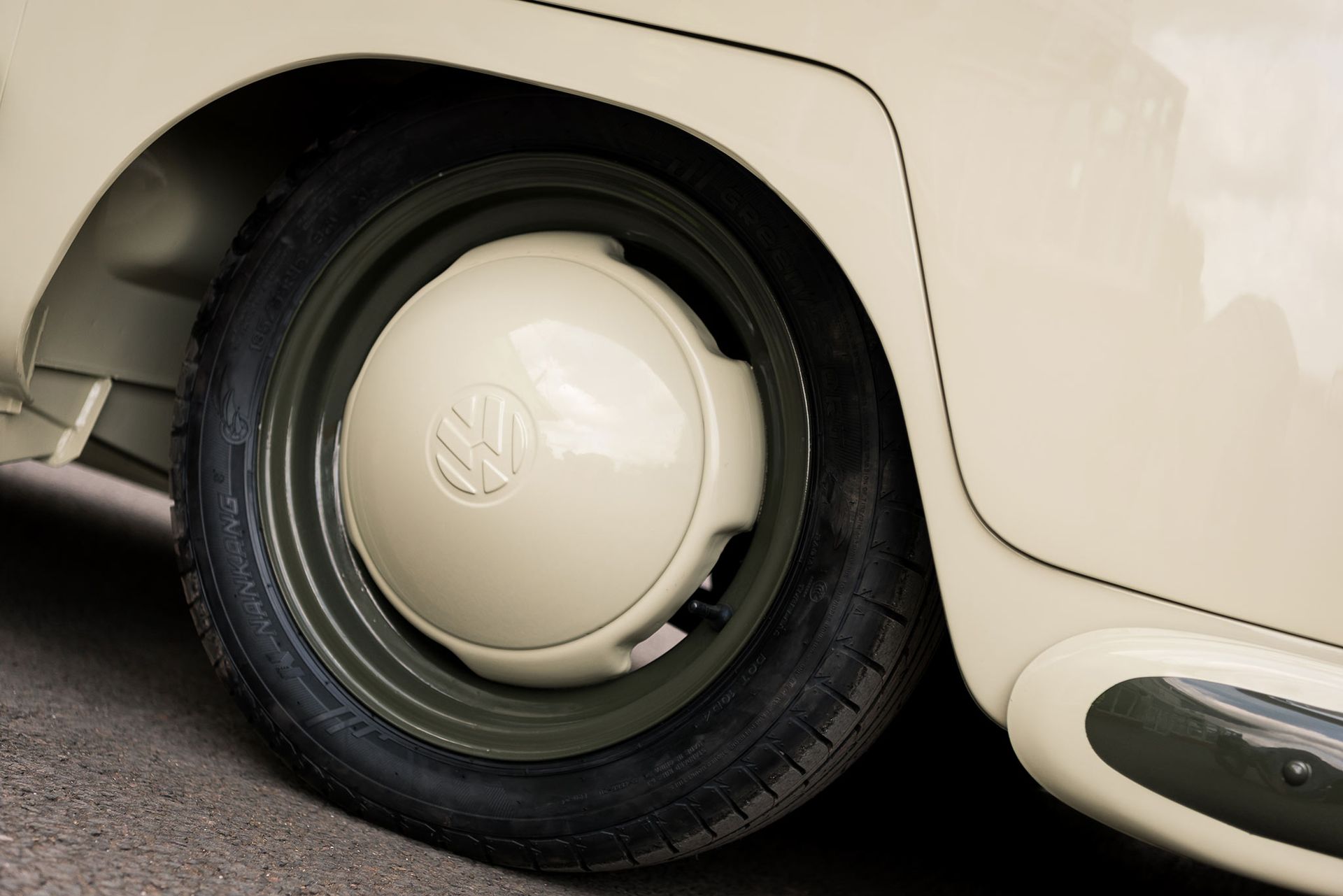 Close-up of a white car’s rear wheel with a cream hubcap and black tire against the body panel.