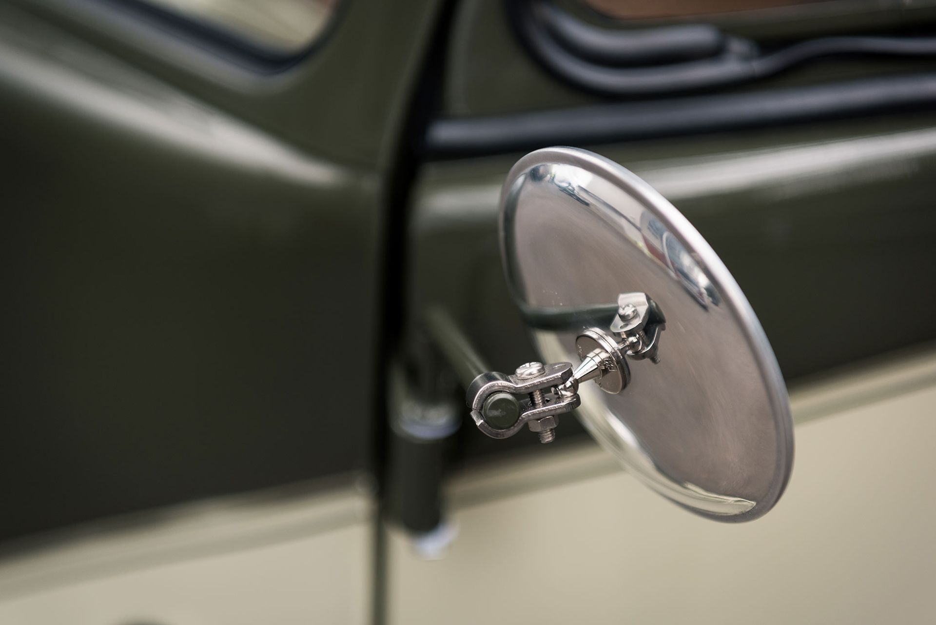 Close-up of a chrome side mirror on a dark green vintage car