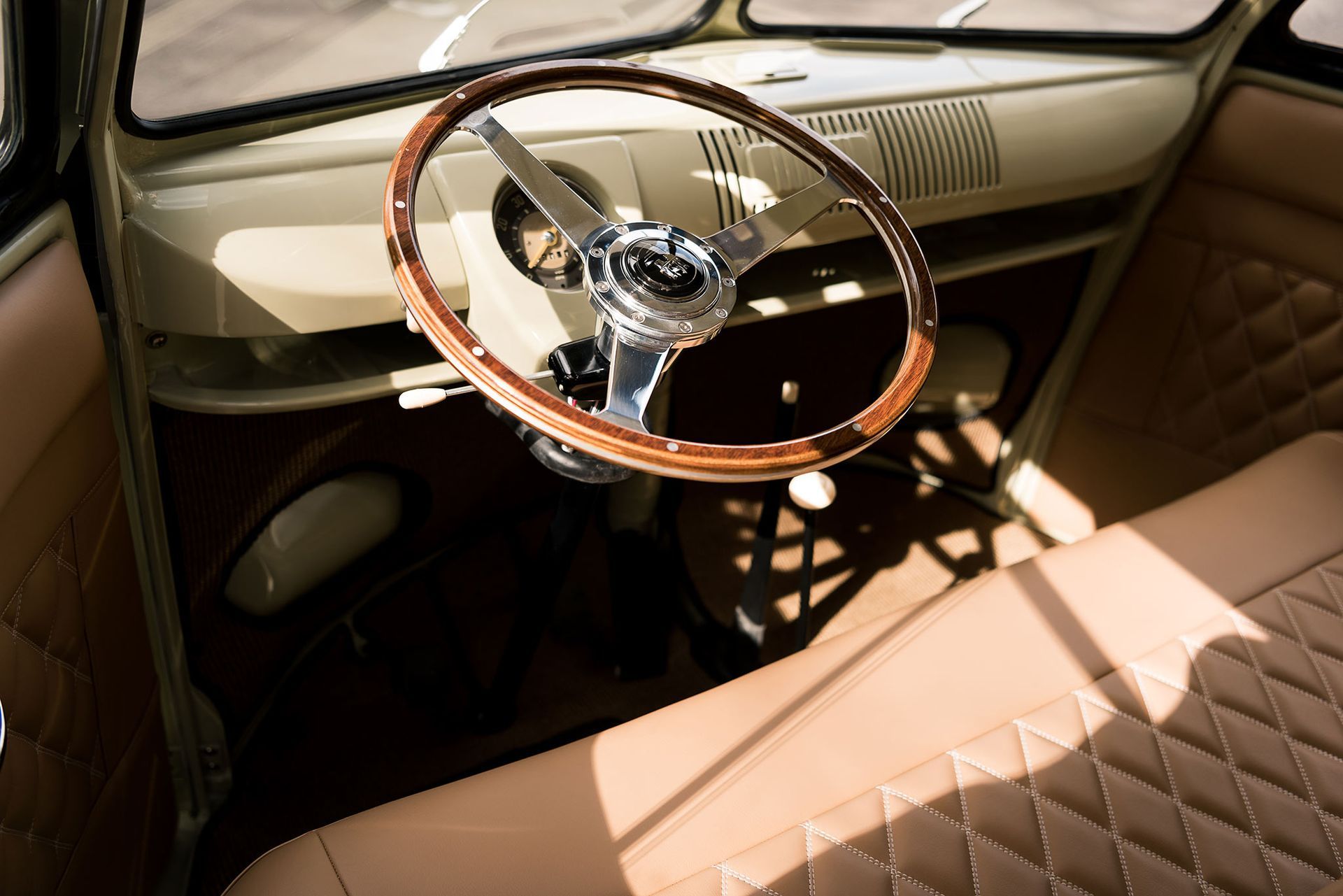 Vintage car interior with tan leather seats and a wood-rim steering wheel in sunlight