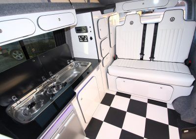 Modern RV interior with white bench seating, black-and-white checkered floor, and compact kitchen counter