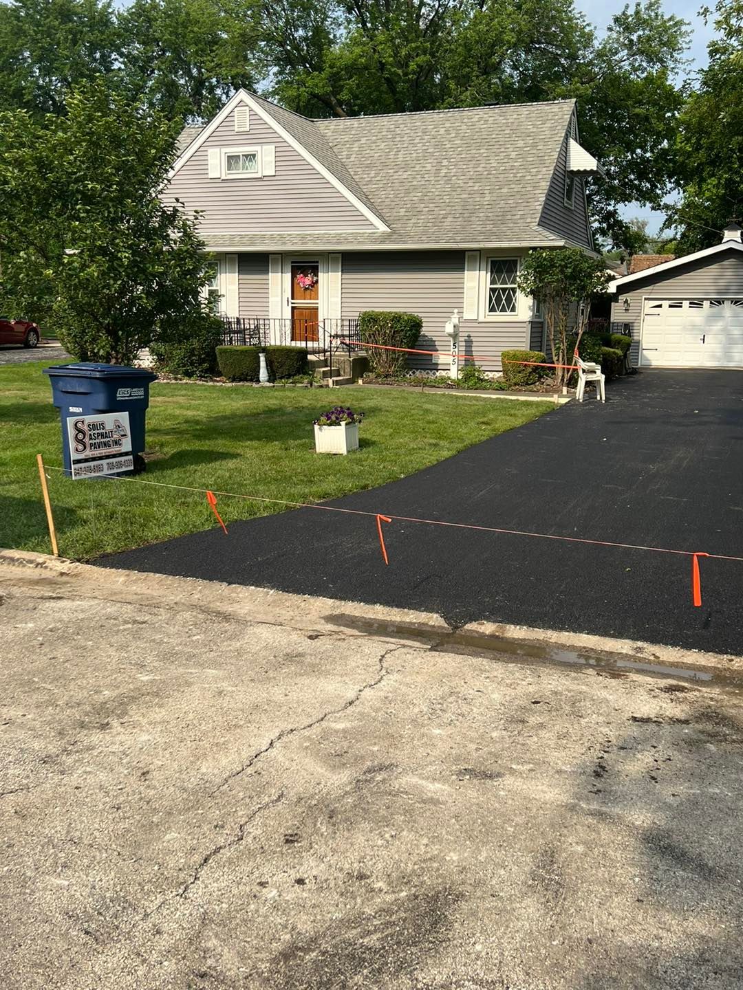 Suburban house with freshly paved black driveway and a real estate sign in the front yard