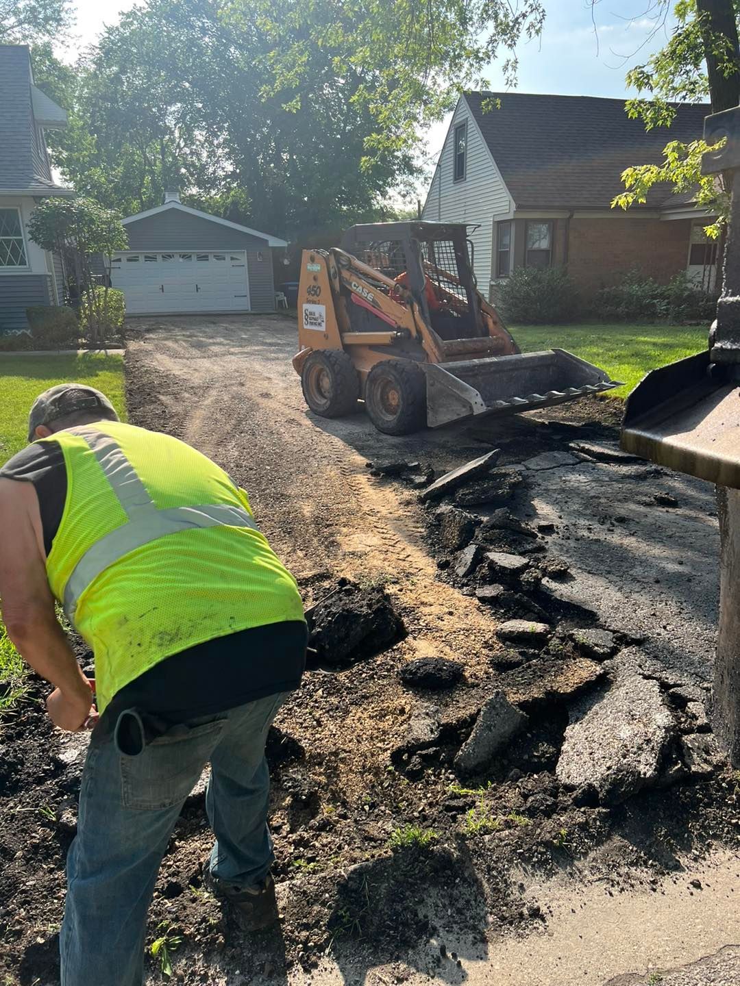 Road work crew clearing broken pavement with a skid steer on a residential street