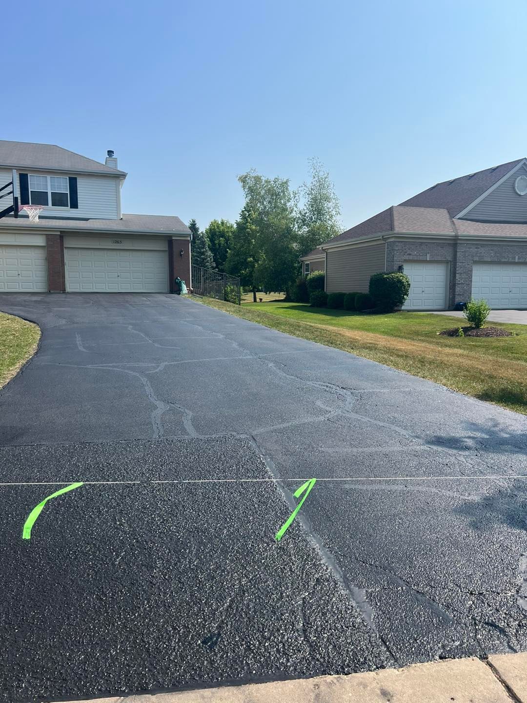Residential driveway under construction with dark asphalt and green spray markings between houses on a sunny day