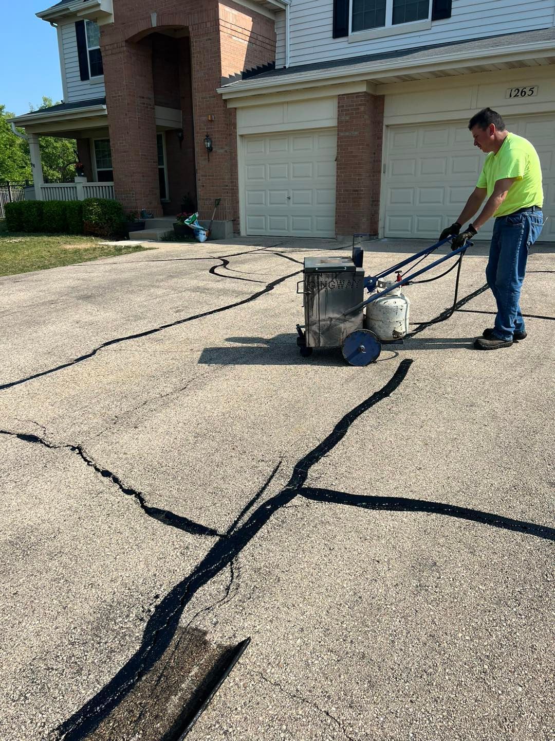 Man using a crack-sealing machine on a cracked driveway beside a house