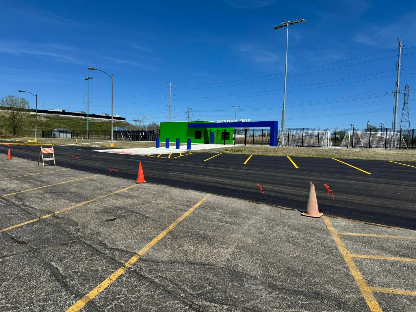 Empty parking lot with orange cones and a small green-and-blue building in the distance