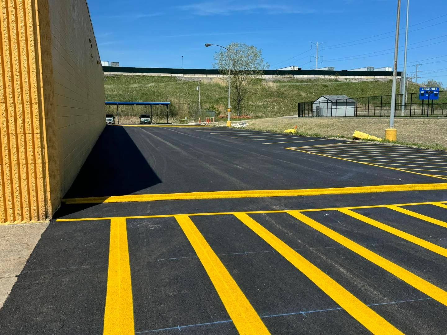 Empty asphalt lot with bright yellow parking lines beside a tan building and overpass in the distance