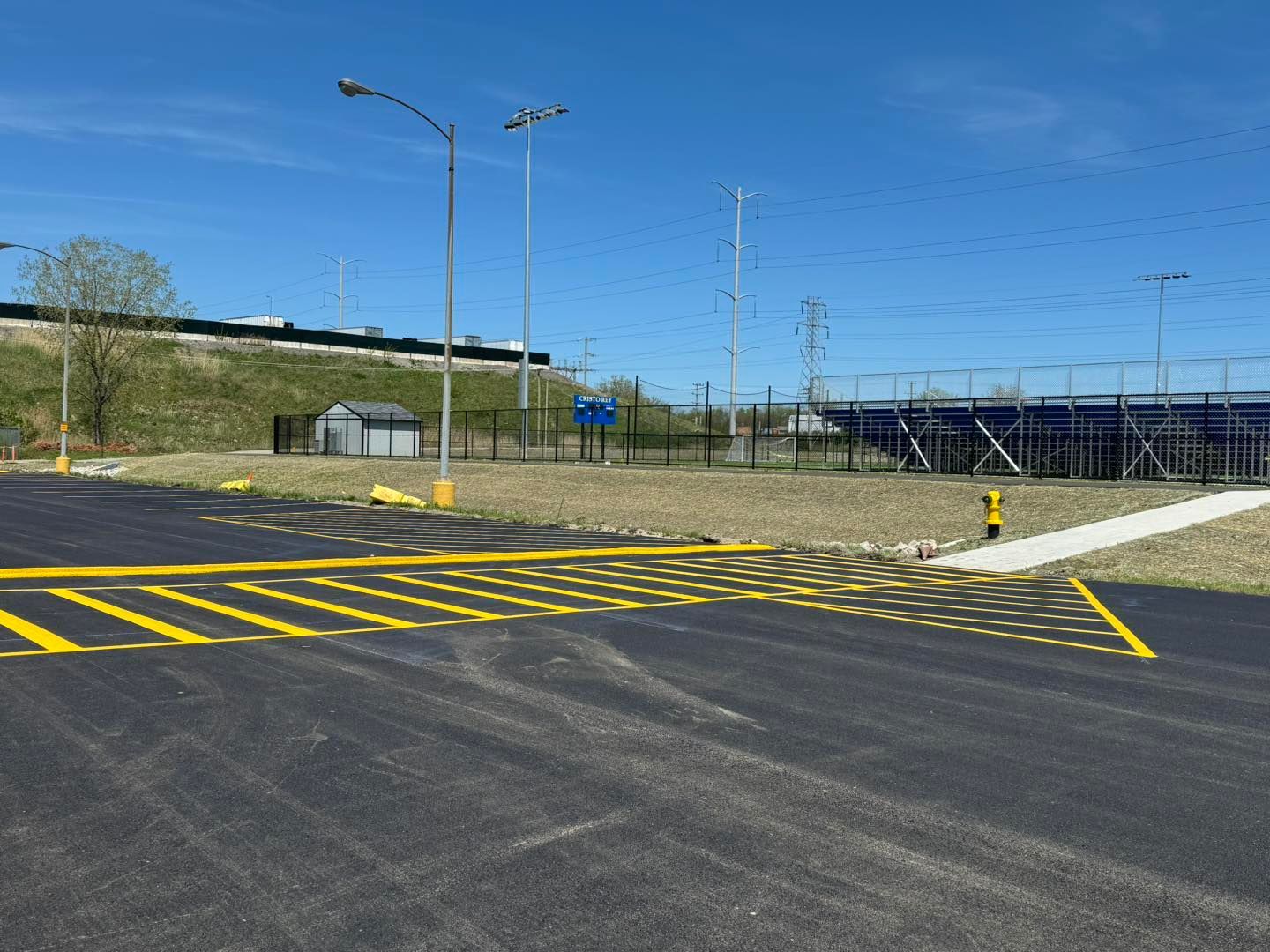 Empty road intersection with yellow crosswalk markings, streetlights, and a fenced area under a clear blue sky