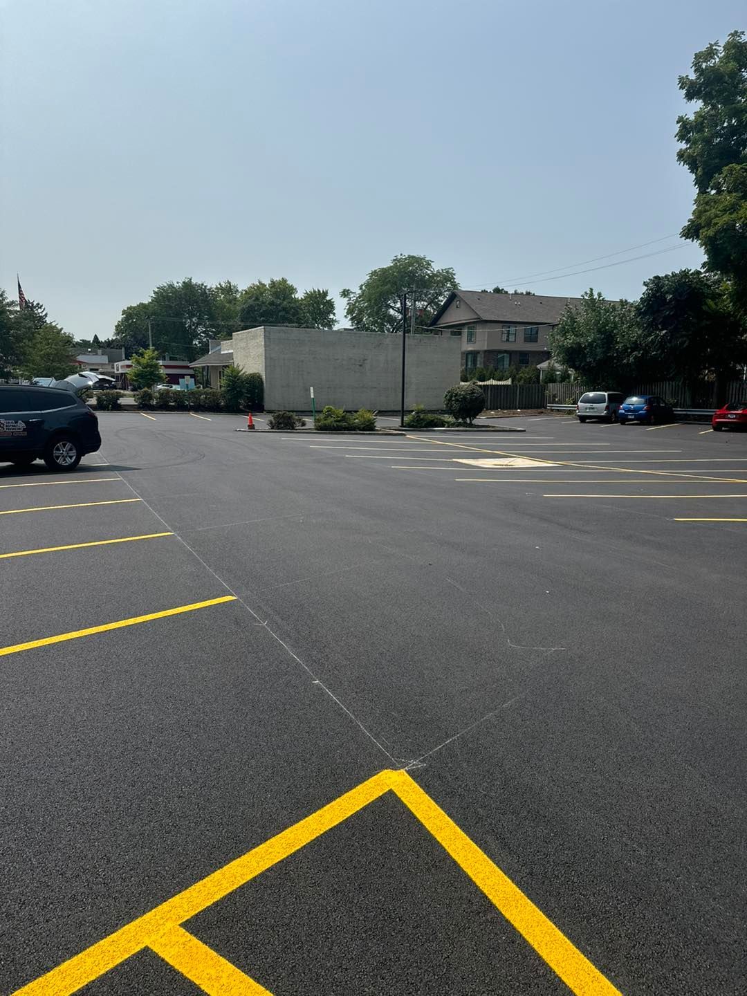 Empty parking lot with yellow lines, parked cars, trees, and a white trailer under a sunny sky
