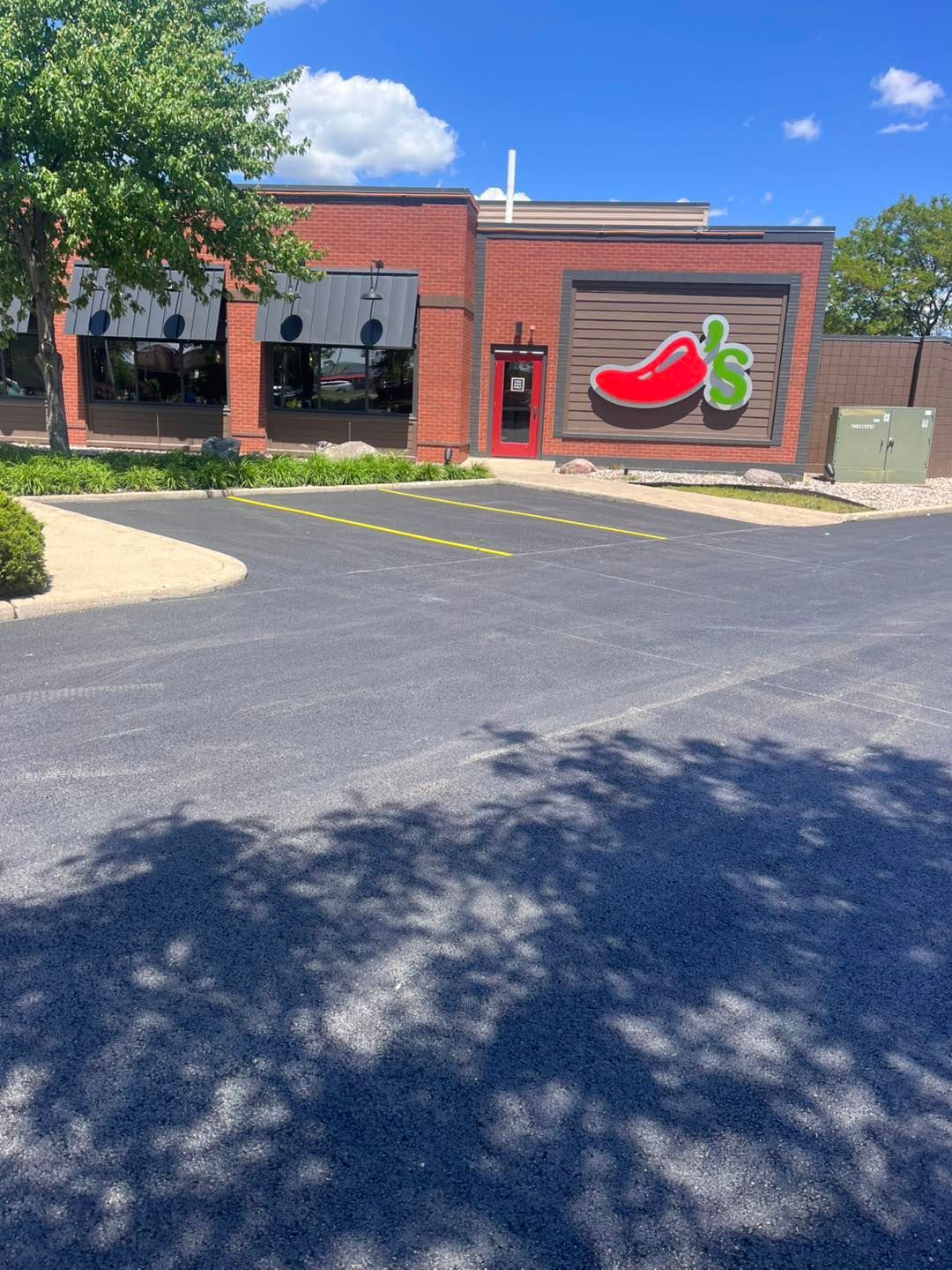 Brick storefront with a red chili pepper sign, glass windows, and parking lot in front