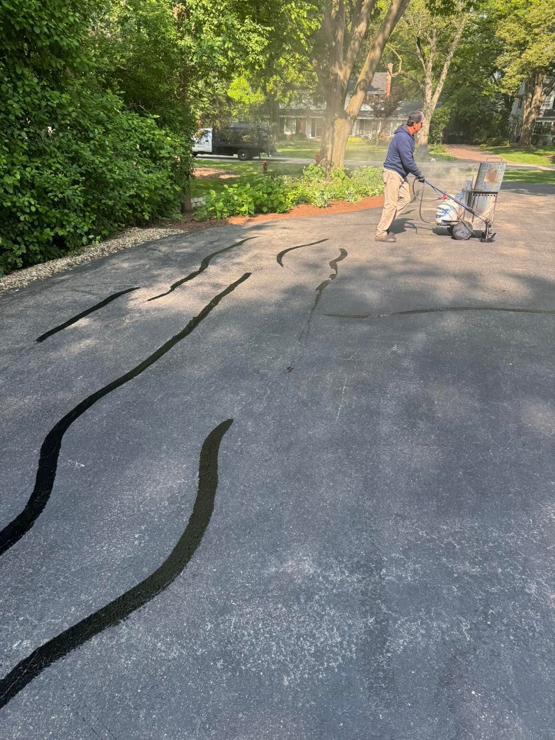 Person pushing a cart on a cracked driveway beside trees and greenery
