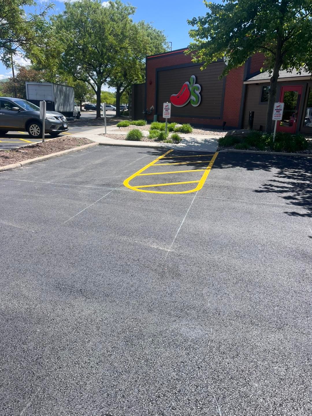 Parking lot with yellow-outlined accessible space near a brick building with a cherry logo.