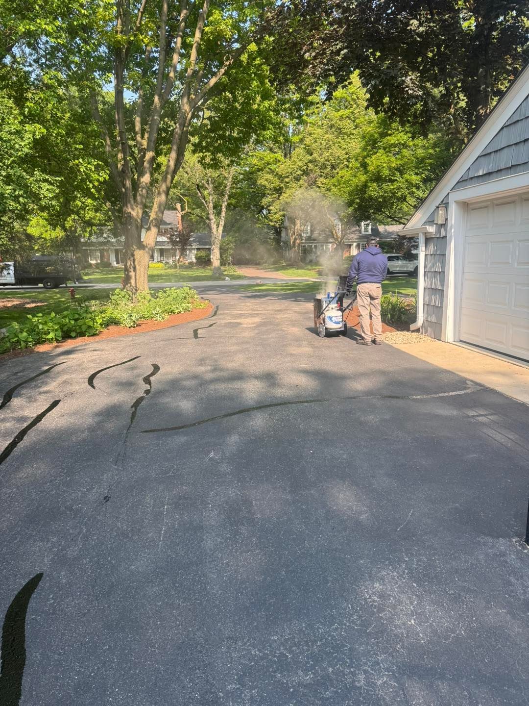Driveway beside a garage with two people near a cart, trees and flower bed in the background.