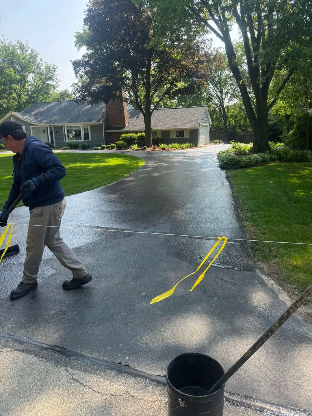 Person pressure-washes a driveway beside a house, with wet pavement and yellow markings.