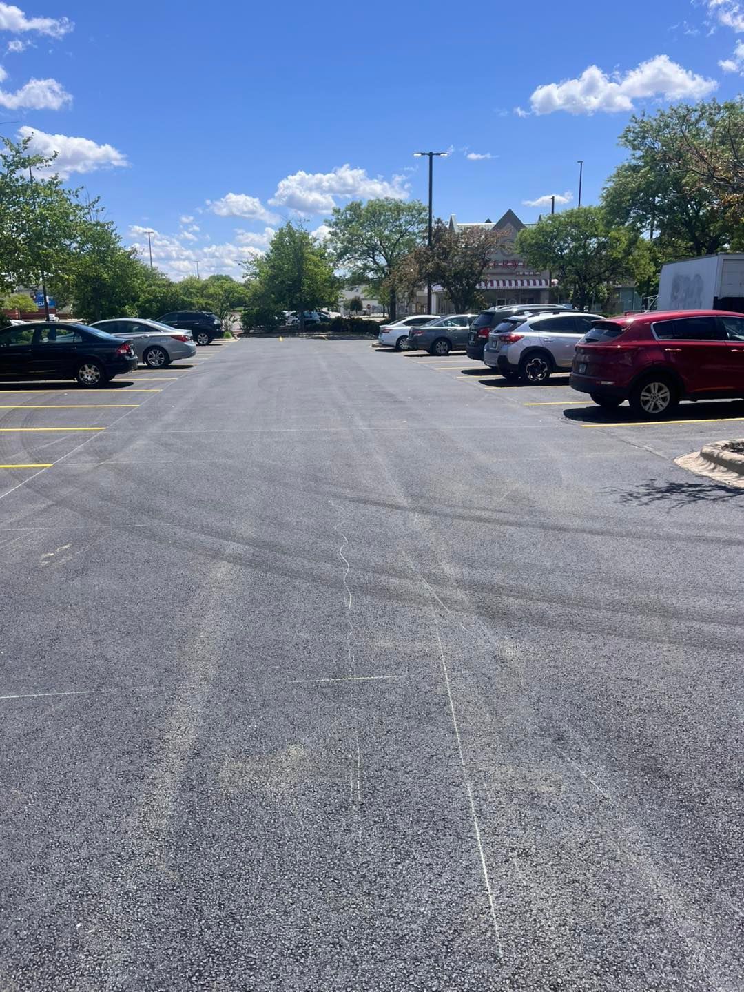 Parking lot with cars on both sides under a sunny blue sky with scattered clouds.