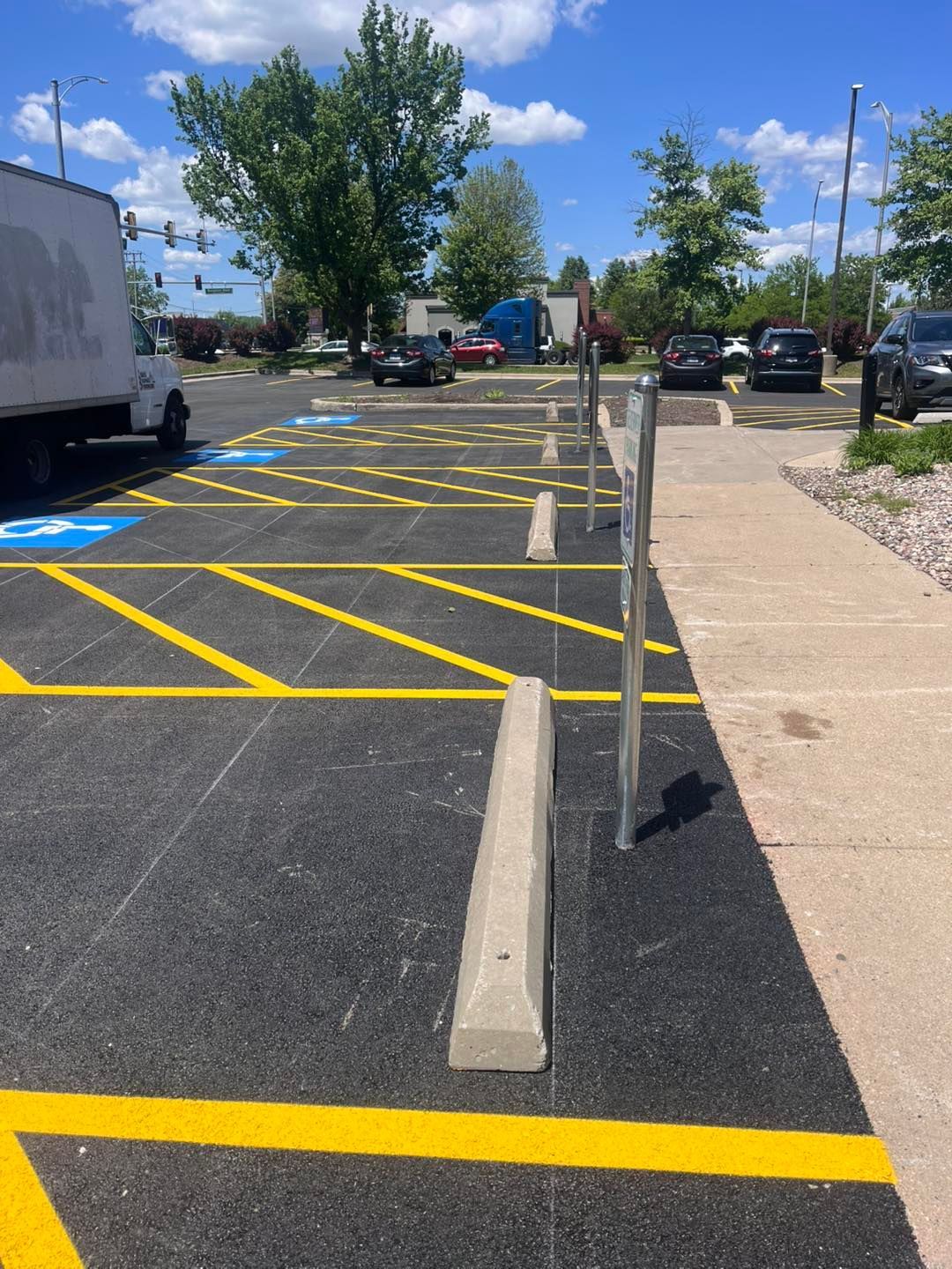 Accessible parking spaces with yellow striping and concrete bollards beside a sidewalk on a sunny day