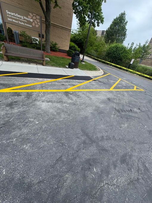 Empty parking lot with yellow striped no-parking zone beside a brick building and trees