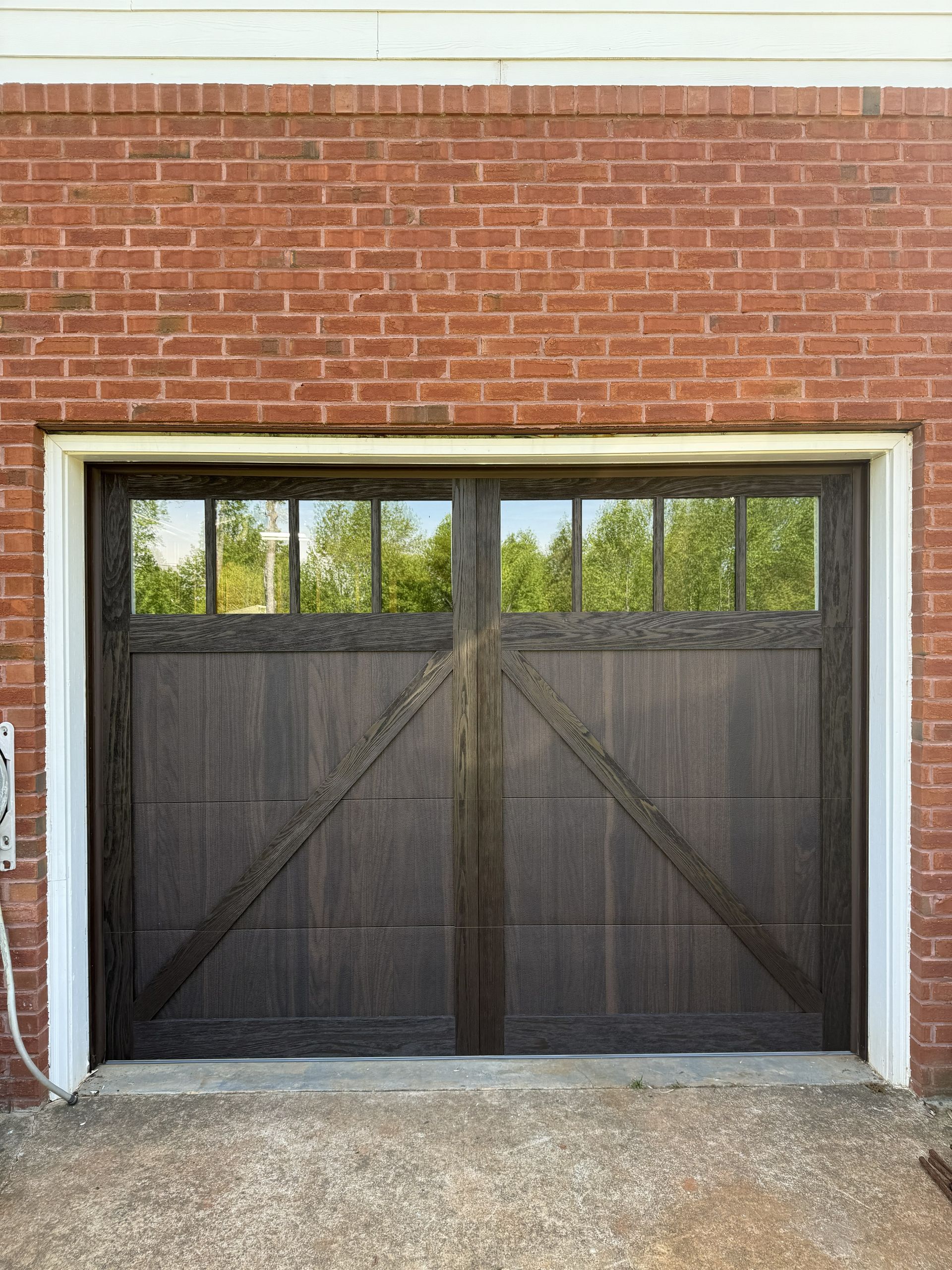 Dark brown garage door with windows, set in a red brick building, concrete ground, white trim.