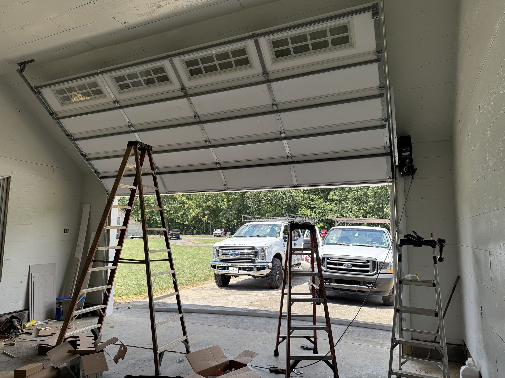 Garage door partially open; two trucks parked outside. Ladders inside, construction in progress.