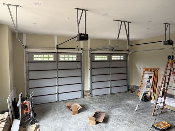 Two garage doors installed in a freshly-built garage with open boxes, ladder, and tools.