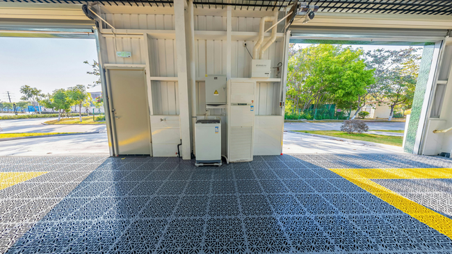 Interior of a white utility structure with electrical equipment; open doors reveal outdoor scenery, yellow stripe on floor.