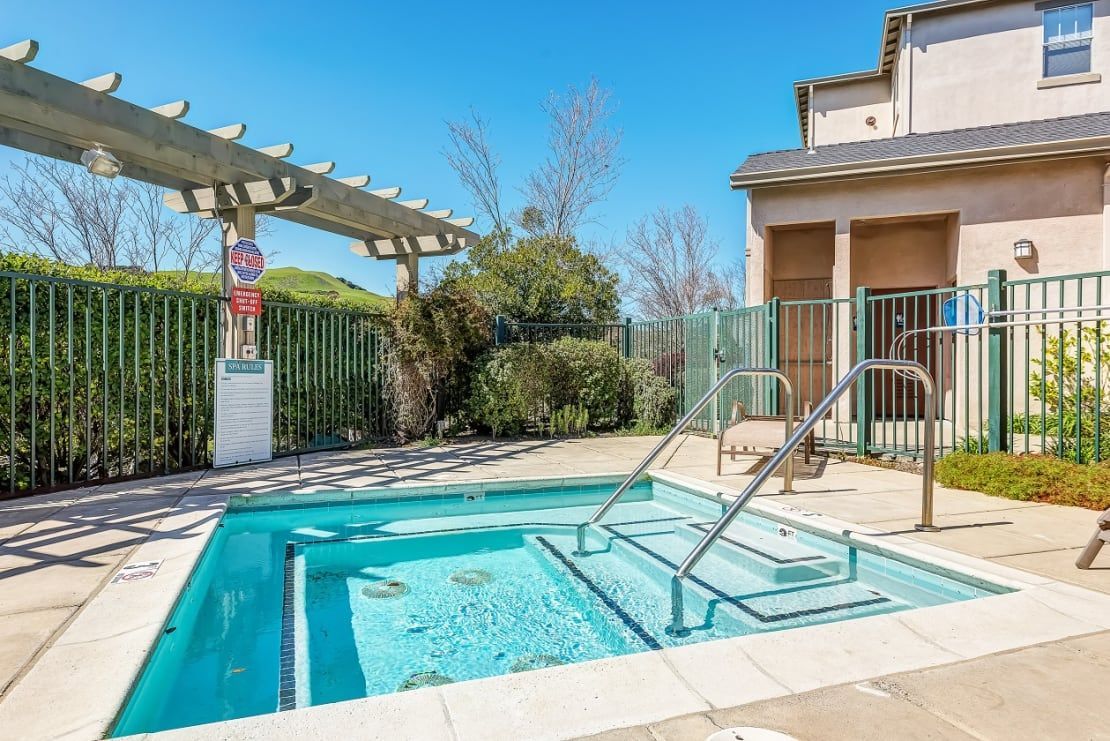 Outdoor backyard pool with metal handrails, patio, and house in bright sunlight