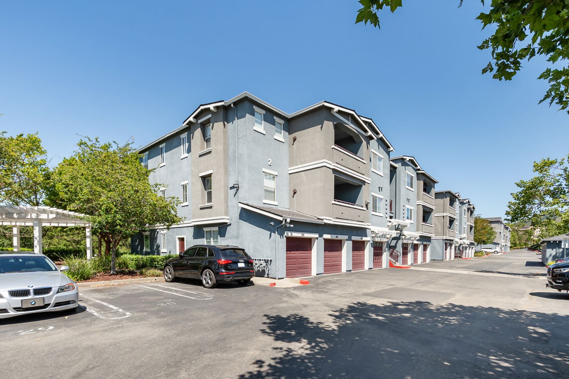 Exterior view of apartment buildings with private garages, mature landscaping, and on-site parking.